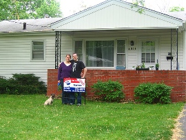 new homeowners outside of house with realtor sign